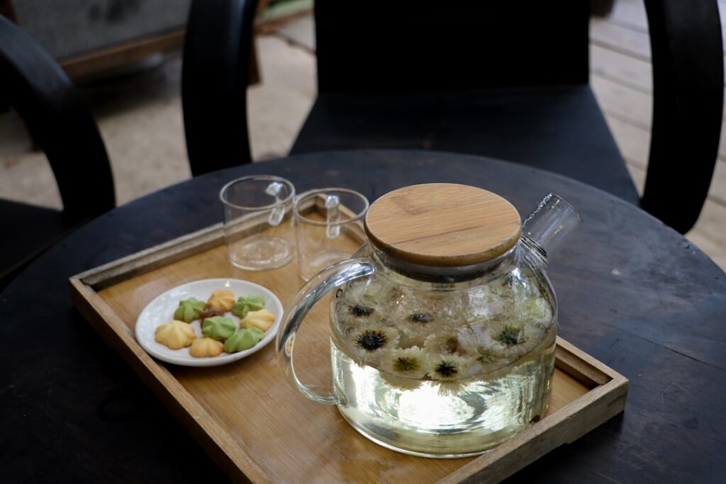 A glass of water with sliced okra and whole cloves steeping in it on a natural wooden surface