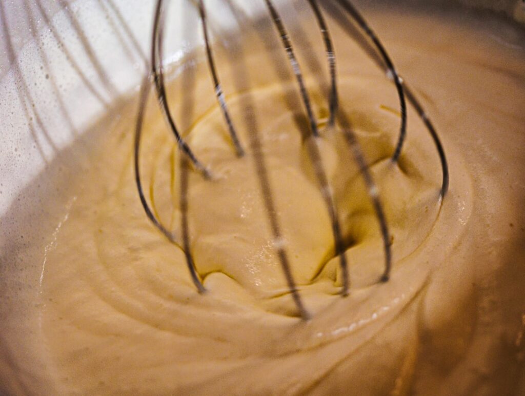 A close-up of a bowl with the DIY glow mask mixture being whisked showing the creamy texture of the egg and petroleum je