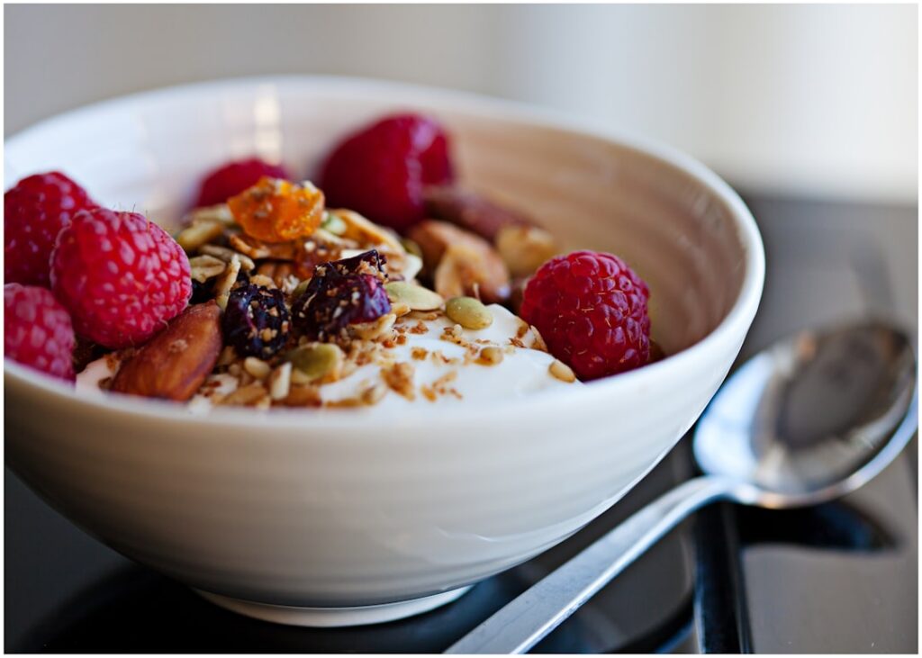 A beautiful bowl of oatmeal topped with fresh berries sliced banana and chopped nuts with a spoon partially in the bowl