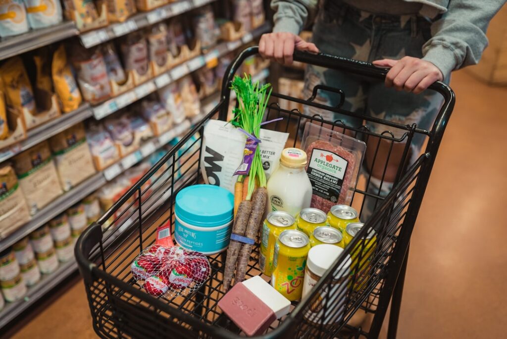 A person s hands holding a grocery basket filled with fresh colorful fruits and vegetables like leafy greens berries and