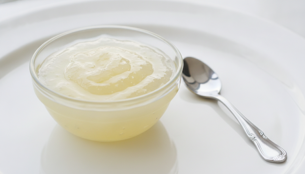 A small glass bowl containing a light yellow gel-like mixture of aloe vera lemon and honey with a spoon beside it