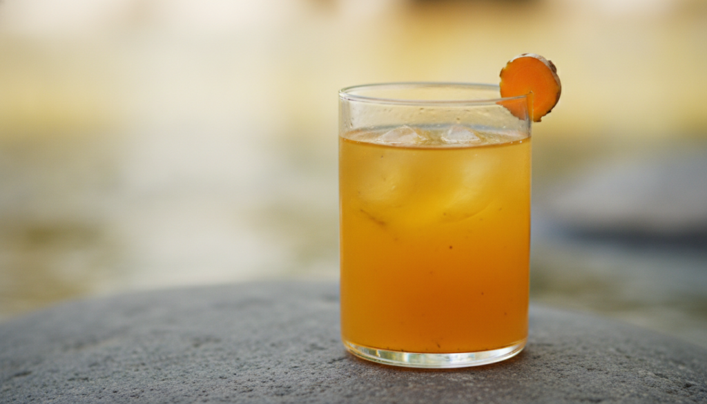 A clear glass filled with the golden-orange joint support tonic garnished with a slice of turmeric or lemon on a natural