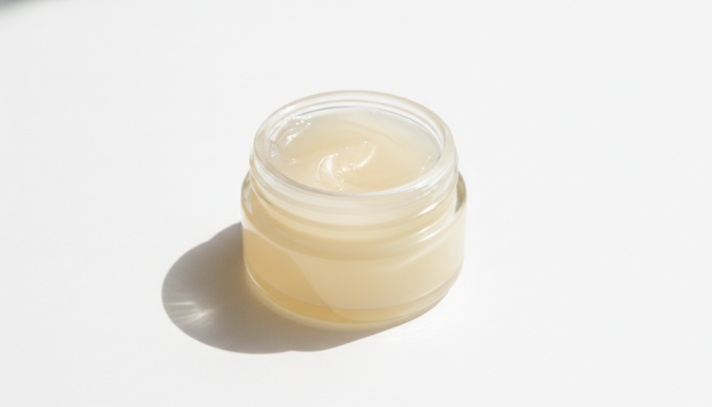 A small open jar of Vaseline petroleum jelly on a clean white background with a soft natural light emphasizing its smoot