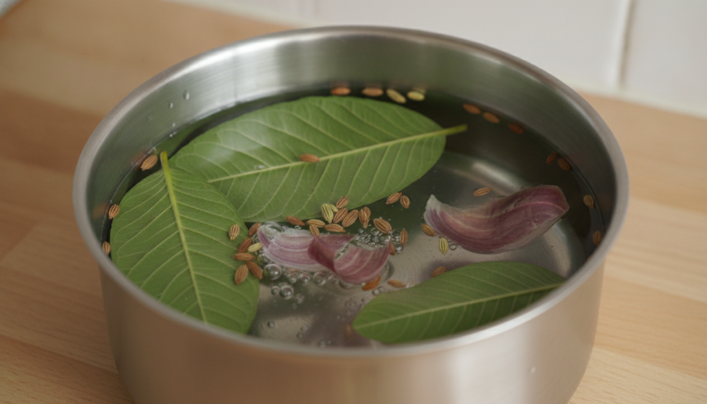 A close-up of fresh green guava leaves whole fennel seeds and reddish-purple onion peels in a small saucepan with water 