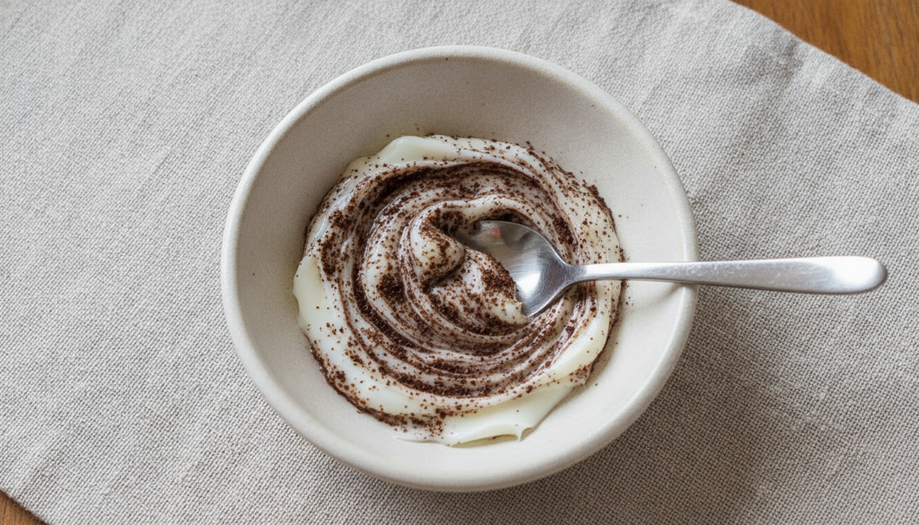 A close-up shot of a small bowl with Vaseline and finely ground coffee being mixed into a paste with a spoon