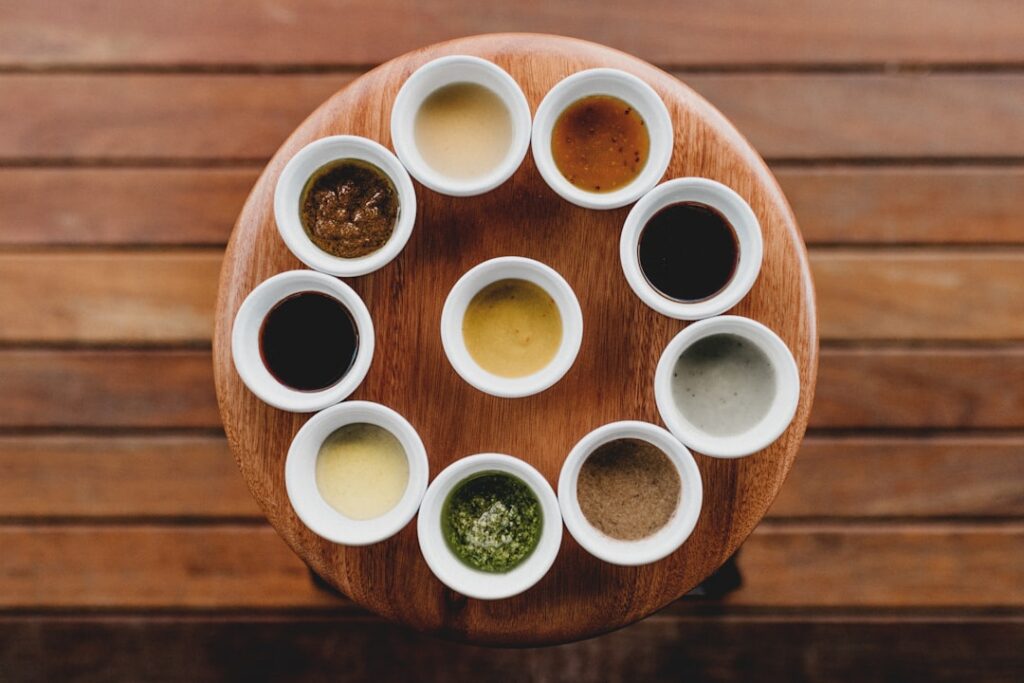 An overhead shot of six small bowls each containing a different colored pizza sauce red marinara green pesto creamy whit