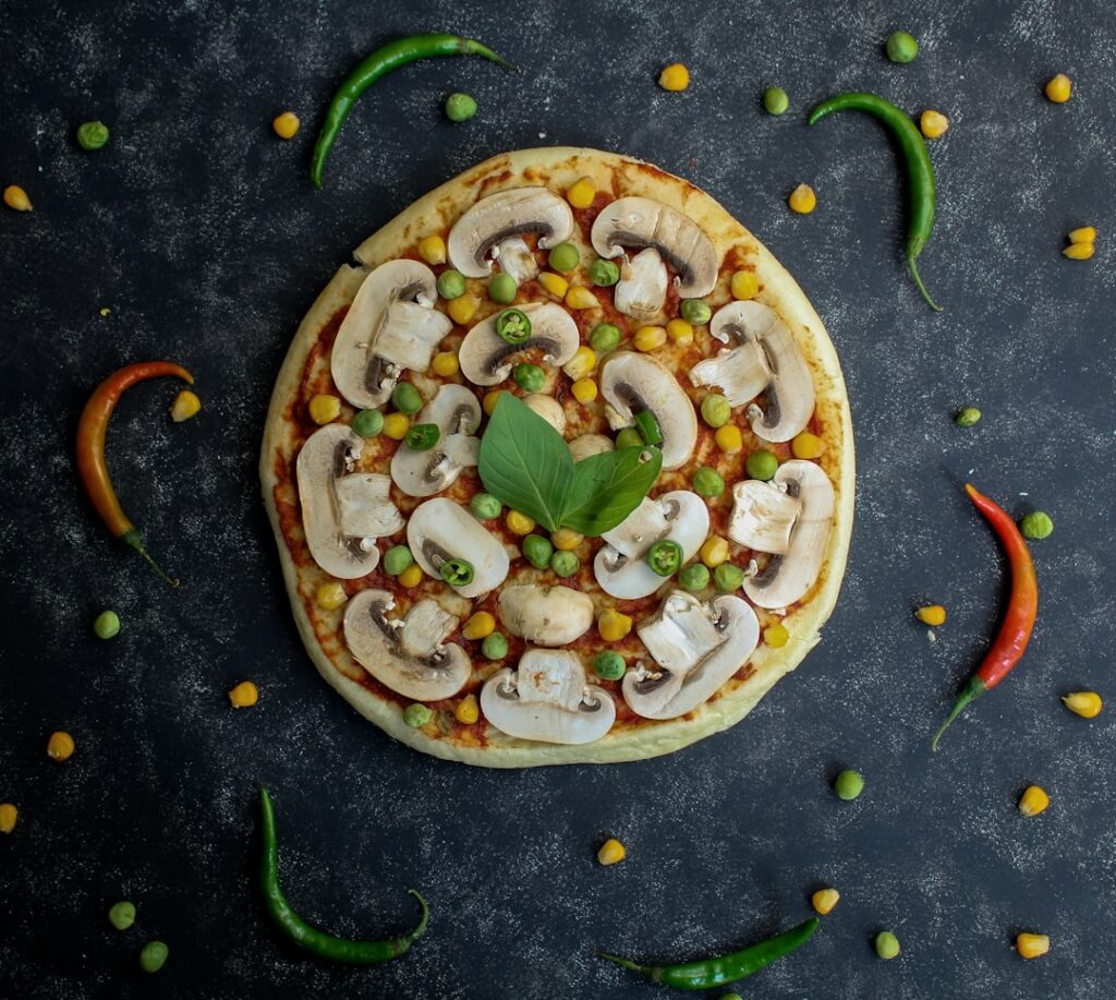 A close-up of a creamy white garlic pizza sauce in a small ceramic bowl with a whisk resting beside it and a few cloves 