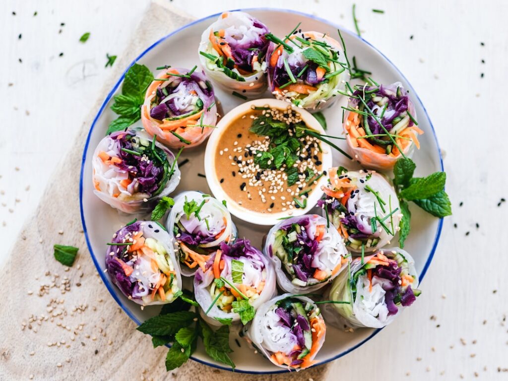 A variety of colorful vegan spring rolls with clear rice paper wrappers showcasing fillings like julienned carrots cucum