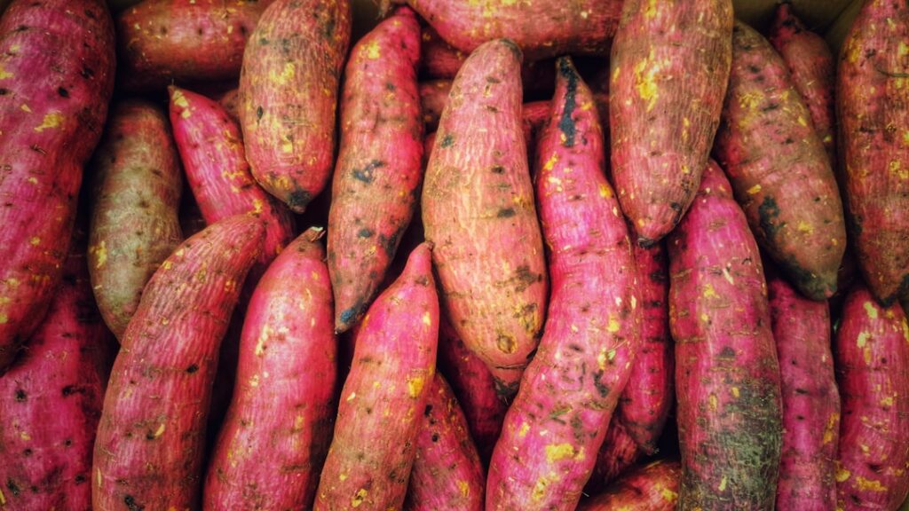 A side-by-side comparison of a raw sweet potato and a raw regular potato on a wooden cutting board highlighting their di