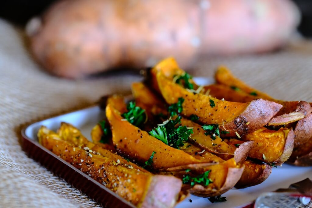A beautifully arranged plate of healthy roasted vegetables including both sweet potato cubes and regular potato wedges s