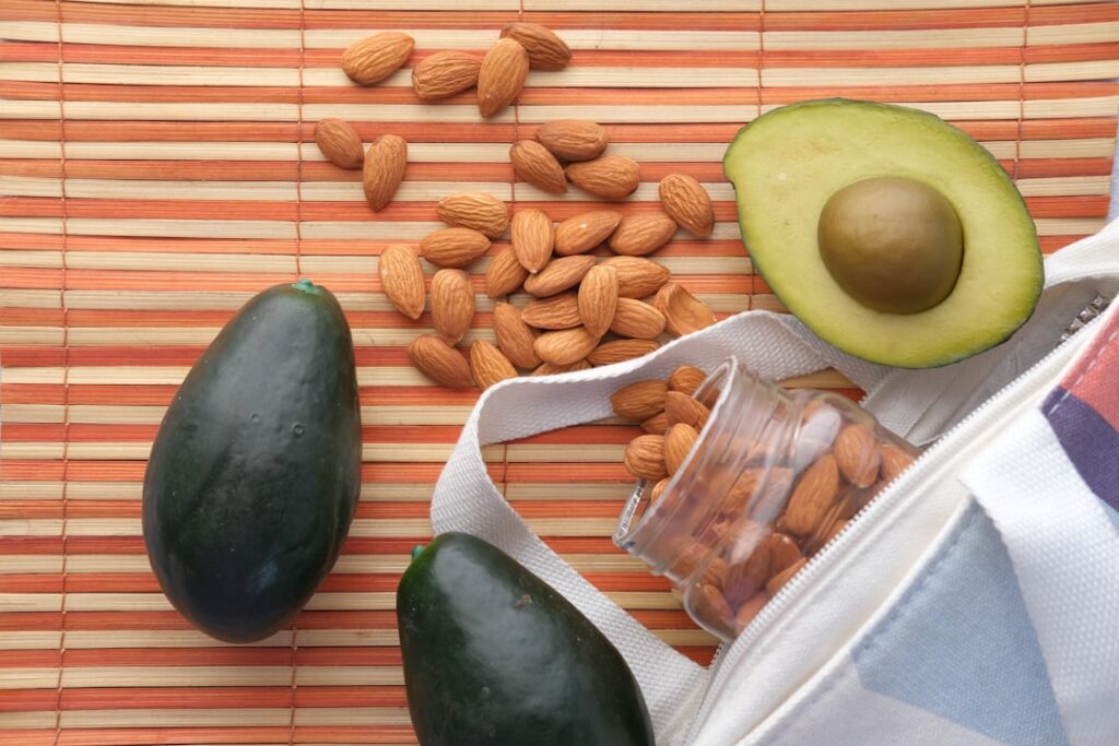 A vibrant and appealing spread of various healthy fat sources including sliced avocado salmon fillet a bowl of mixed nut