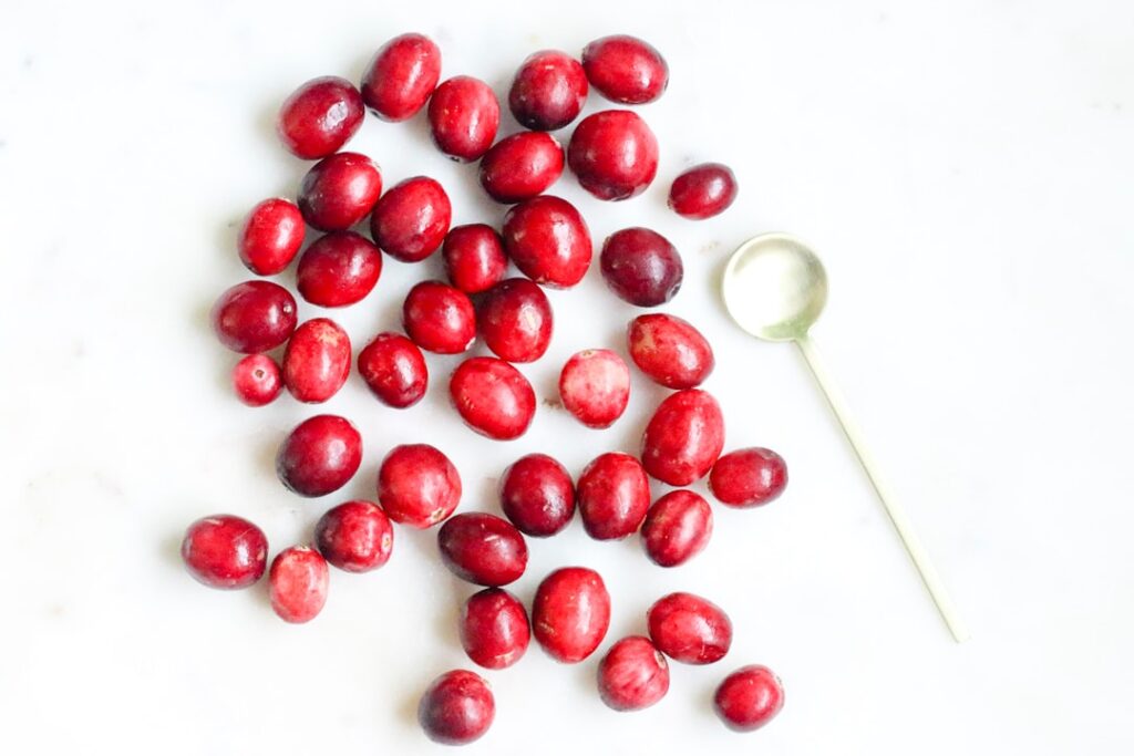 Ingredients for cranberry lemon drink laid out on a wooden table fresh cranberries whole lemons a pitcher of water and a