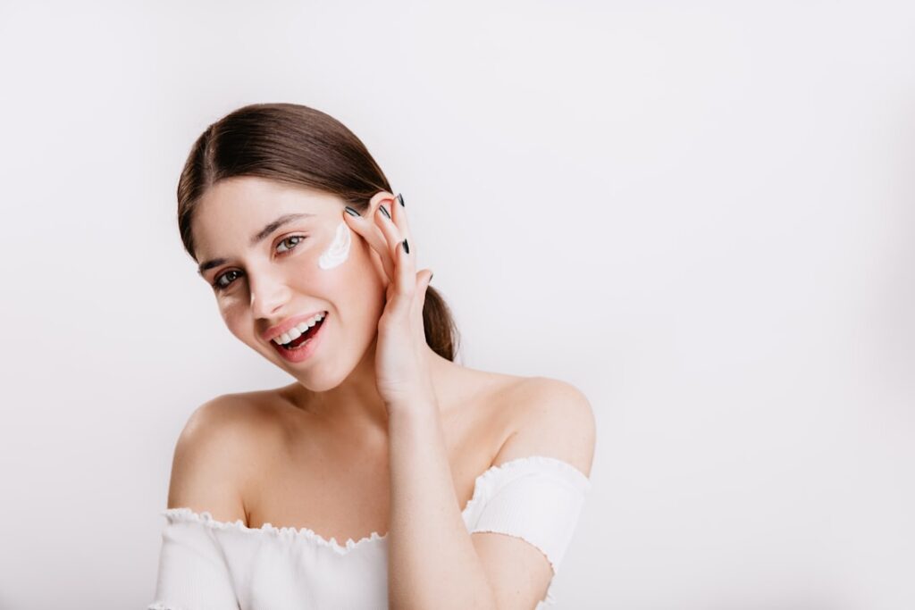 A woman gently applying a clear natural gel to her face smiling softly with radiant healthy-looking skin The background