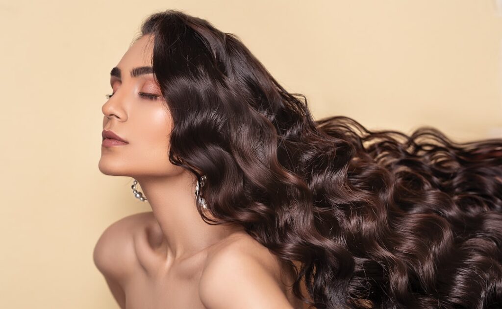 A person with long shiny healthy hair gently running their fingers through it to show its volume and strength The backgr