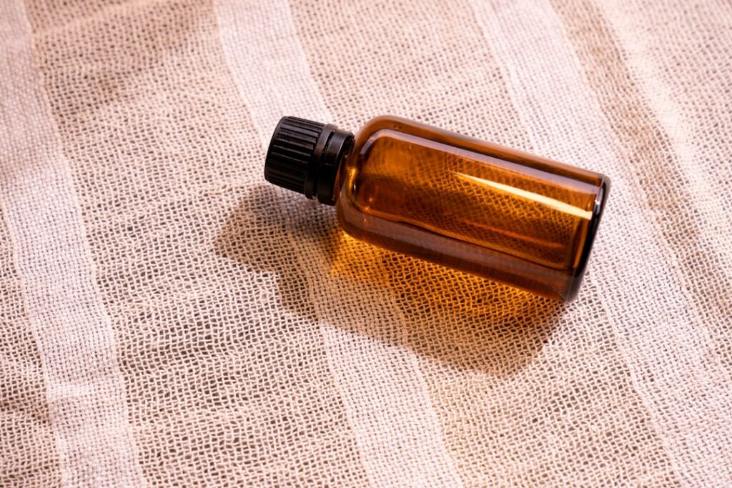 A clear glass spray bottle filled with a light golden liquid labeled Rose Turmeric Toner placed next to fresh roses and 