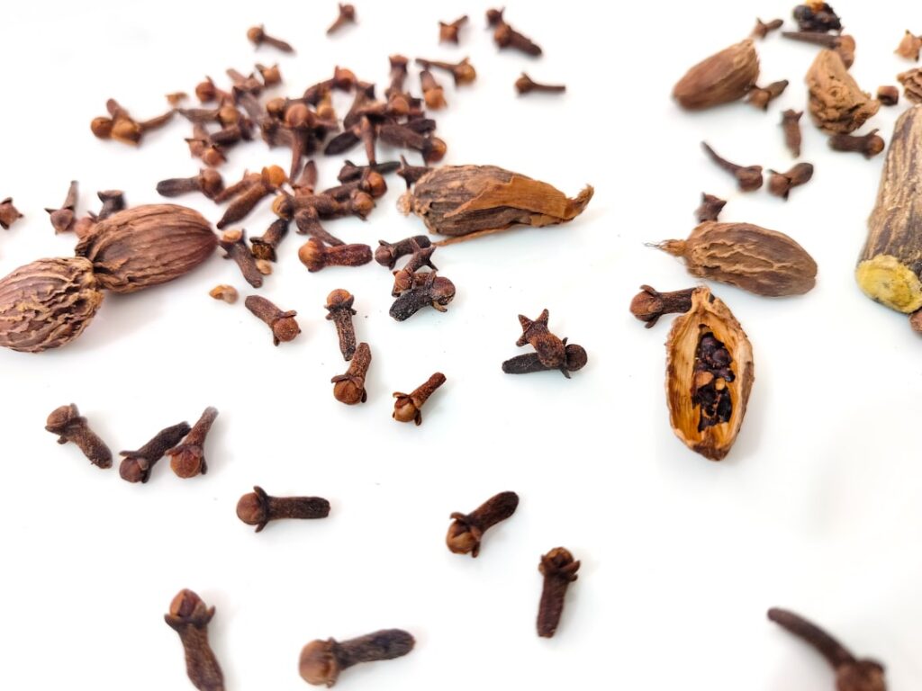 Close-up of whole dried cloves on a rustic surface perhaps with a small bowl of carrier oil in the background hinting at