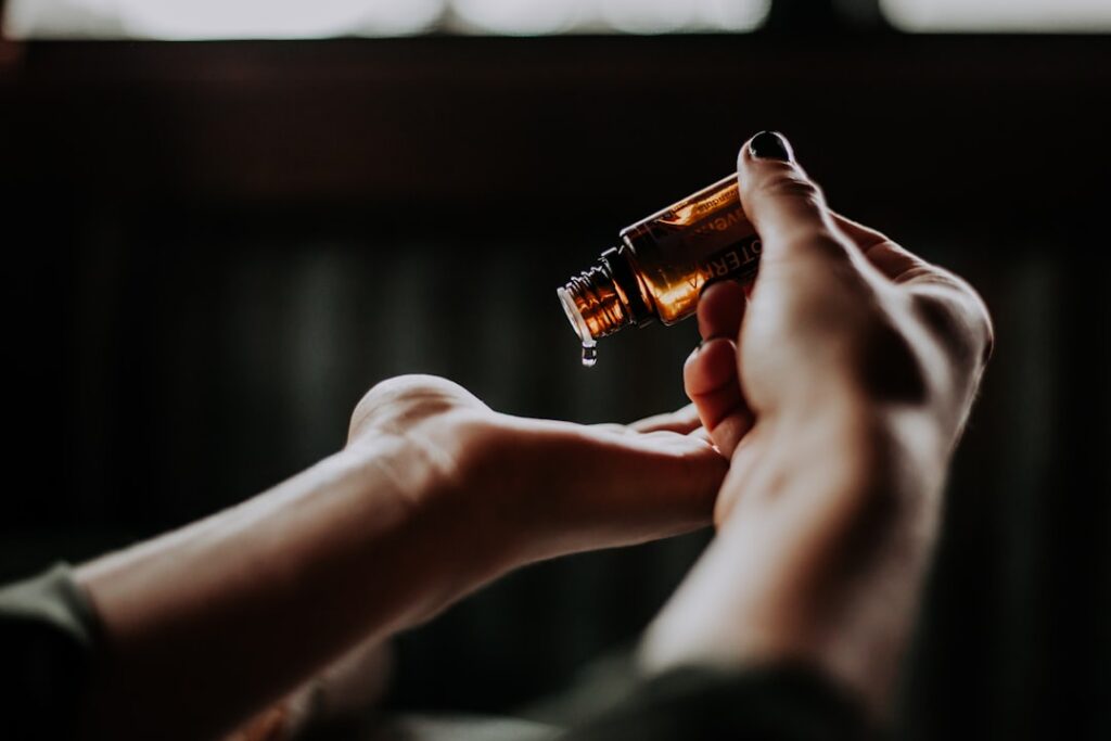 A woman gently applying a drop of DIY facial oil onto her cheek with a dropper in a bright natural setting