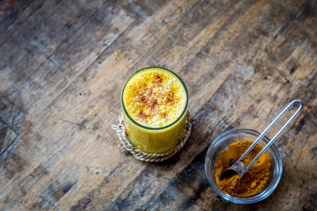 A vibrant golden-yellow drink in a clear glass with visible chia seeds suspended in it There might be a slice of lemon o