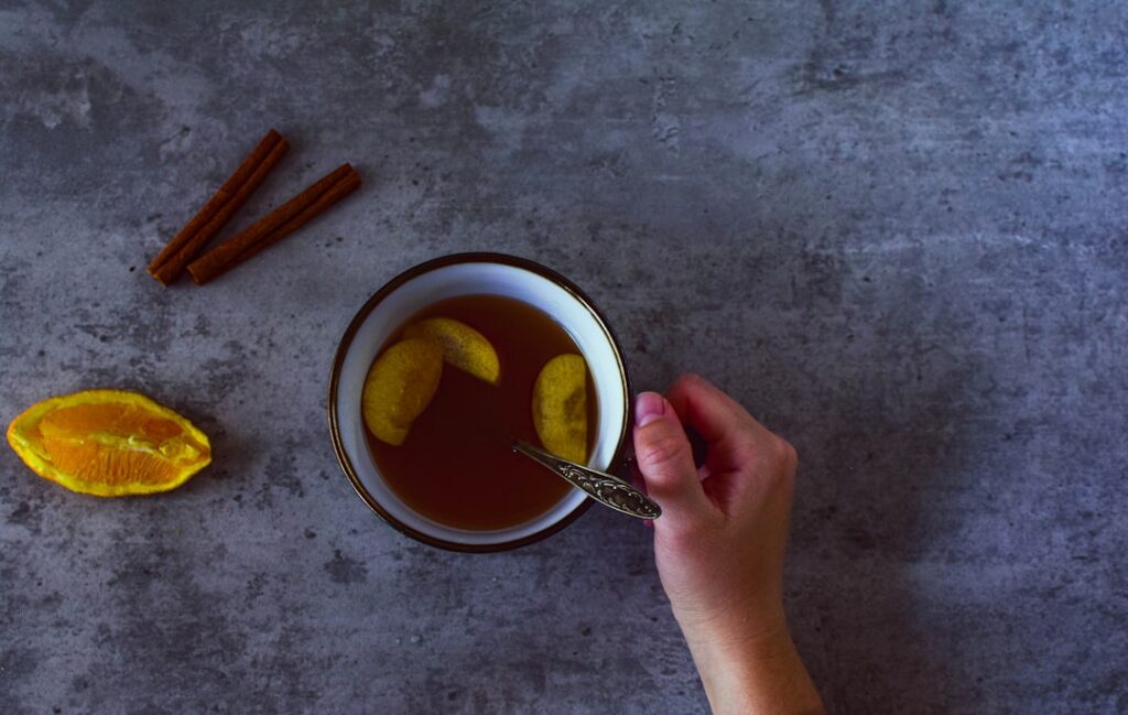 A cozy image of a glass of warm golden-hued drink with whole cloves floating in it perhaps next to a handwritten recipe