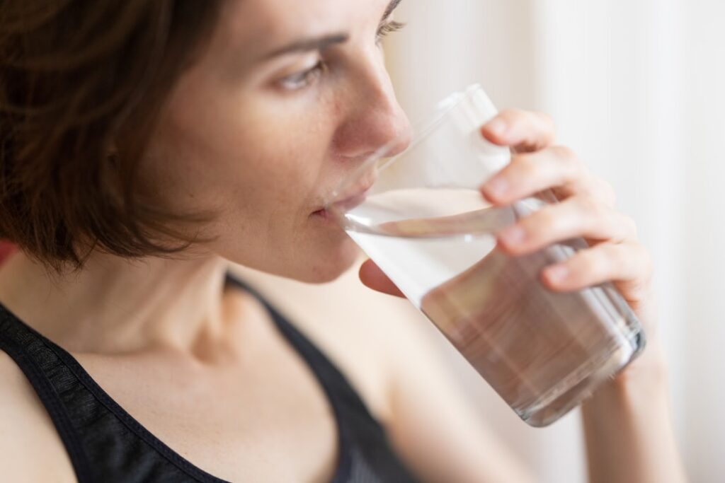 A smiling woman in her 30s or 40s looking refreshed and radiant holding a glass of the clove collagen drink She should c