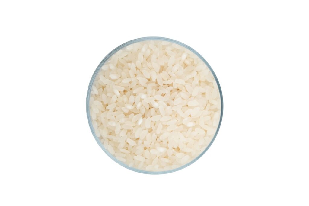 Close-up of white rice soaking in a clear glass bowl with water showing the water turning cloudy