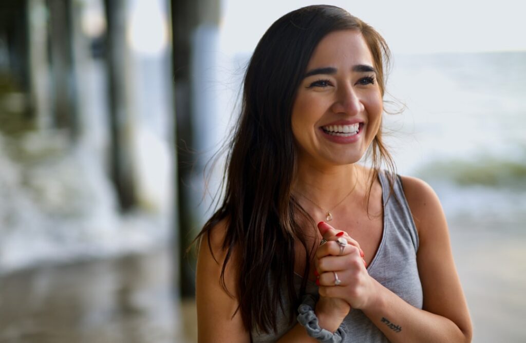 A woman smiling with clear radiant skin holding a glass of green or berry-colored smoothie She looks refreshed and happy
