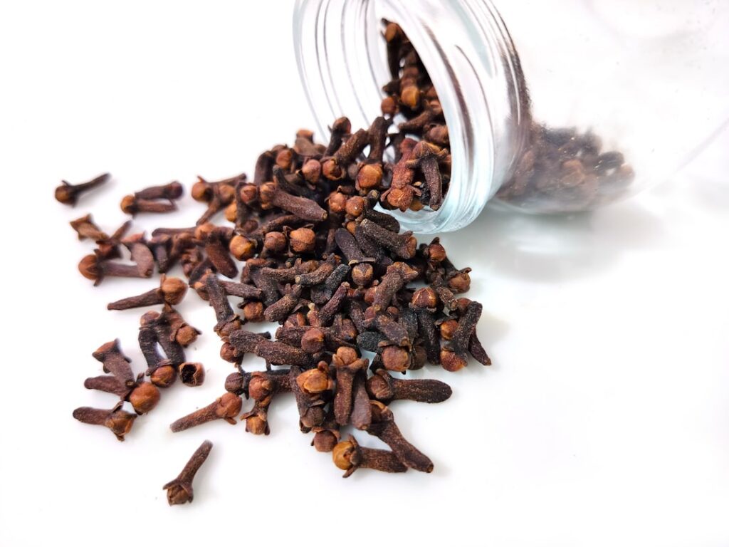 A close-up of dried cloves and a small bottle of clove essential oil on a wooden surface with soft natural lighting
