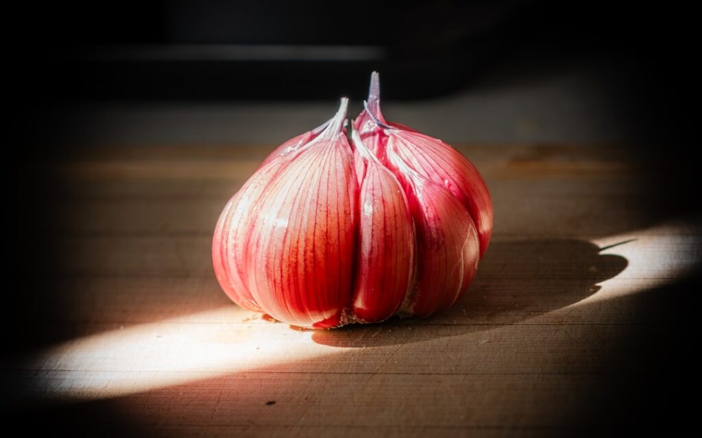 A close-up of a glass bottle of amber-colored homemade onion hair oil with a few red onions and herbs in the background 