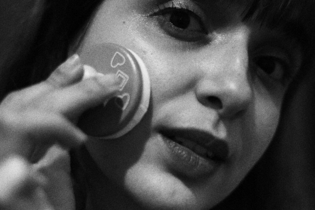 A woman gently dabbing her face with a cotton pad soaked in a homemade toner looking fresh and natural in a brightly lit