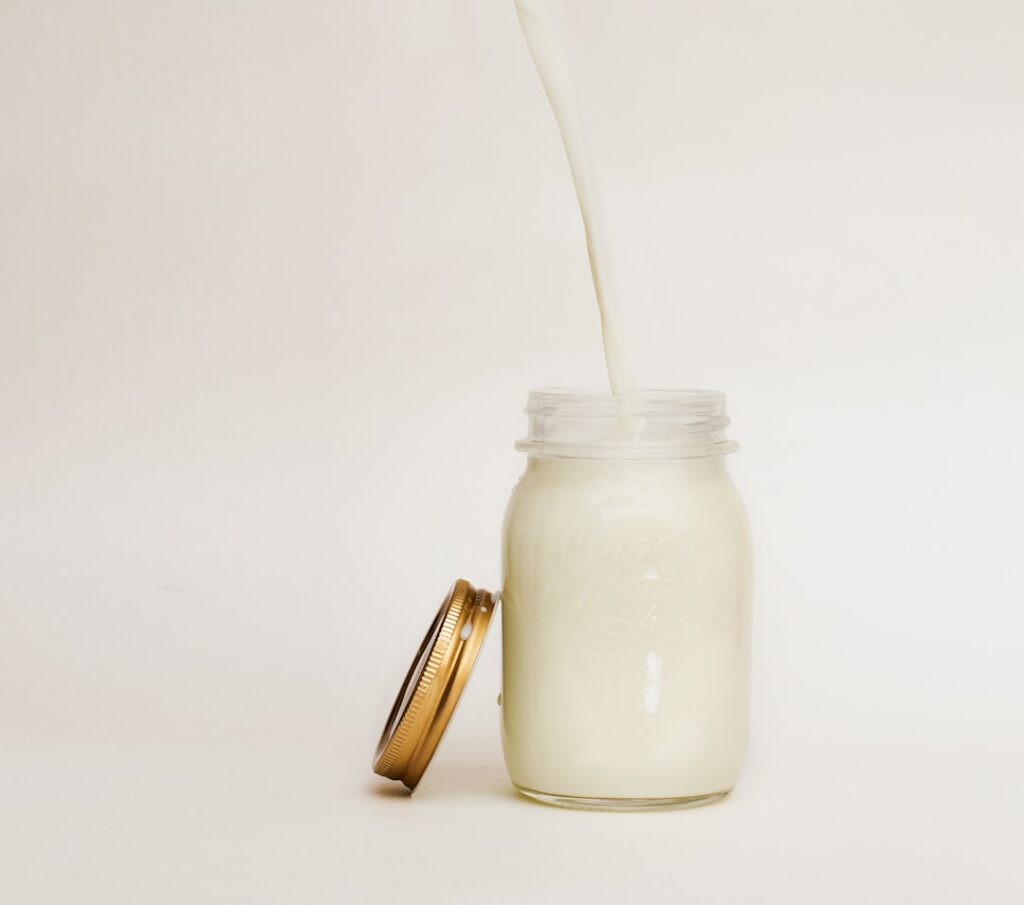 A close-up shot of a small bowl containing a creamy white homemade lotion with a small jar next to it and the ingredient
