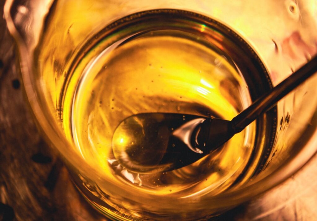 A close-up of a hand mixing ingredients in a small bowl with bottles of baby oil vitamin E capsules lemons and turmeric