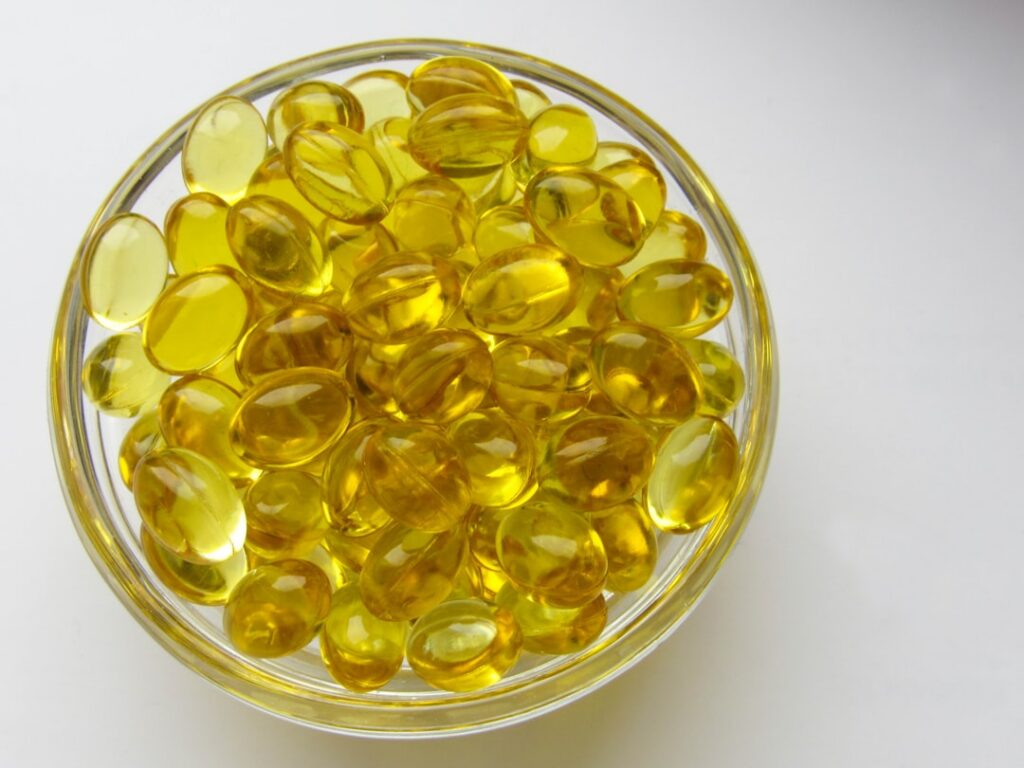 A hand holding a small bottle of baby oil with a green vitamin E capsule next to it against a soft glowing background il