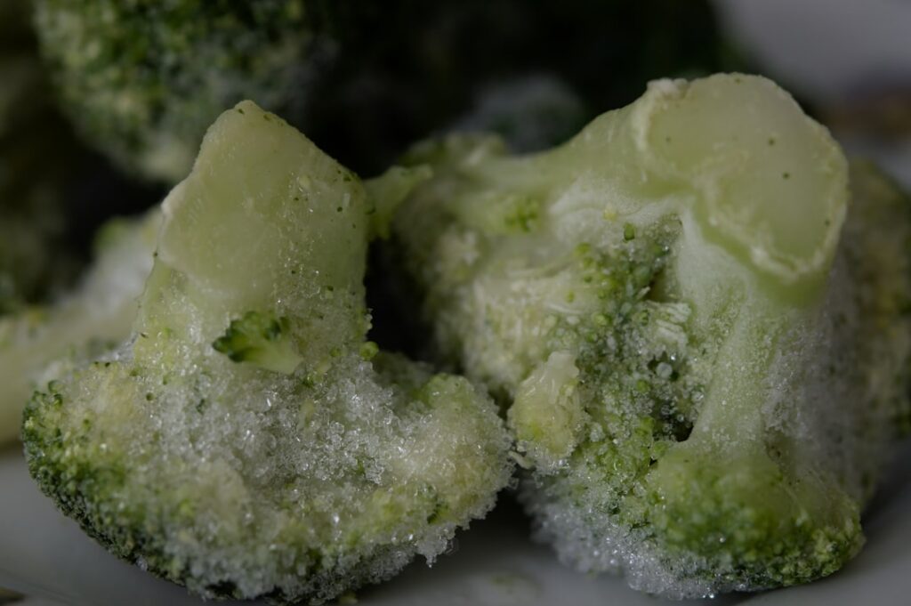 A close-up shot of vibrant blanched broccoli florets and chopped carrots being spread out on a baking sheet ready for fl