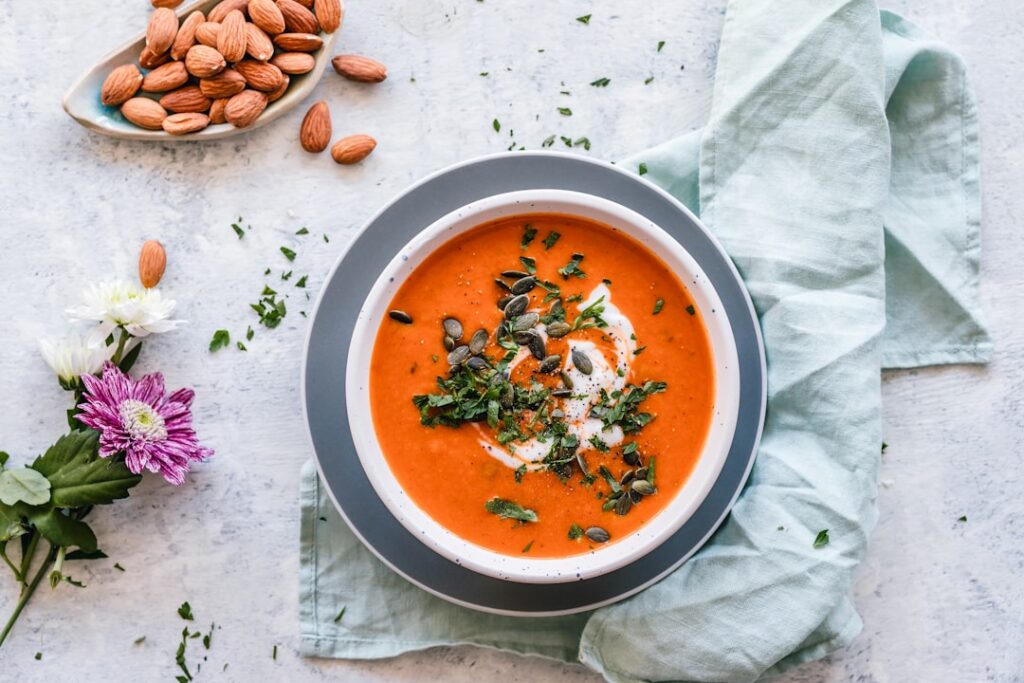A vibrant bowl of creamy roasted red pepper soup garnished with fresh parsley on a rustic table setting