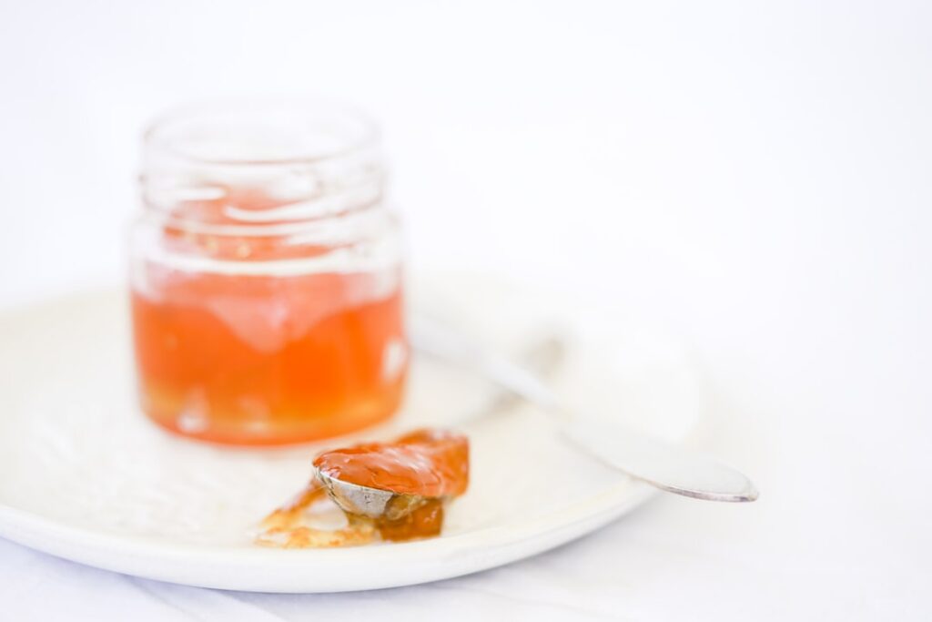 A close-up shot of homemade vegan orange jelly in a small glass jar garnished with fresh orange slices and mint leaves g