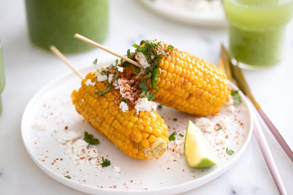 A clear glass cup filled with creamy vegan Mexican street corn esquites garnished with fresh cilantro a sprinkle of red