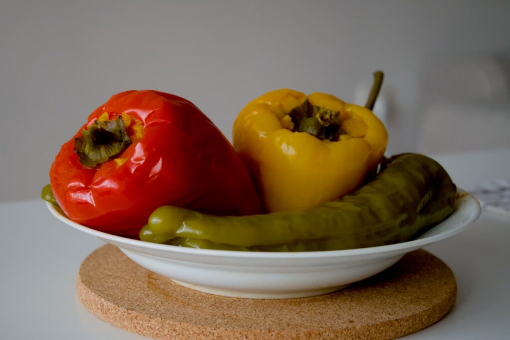 A close-up shot of several vibrant yellow banana peppers some whole and some halved with a bowl of sauerkraut and other