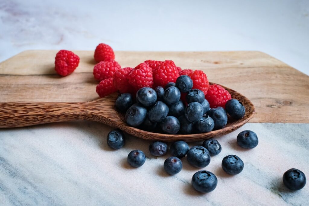 A jar of freshly made vibrant mixed berry jam with a spoon resting in it perhaps on a rustic wooden surface with some fr
