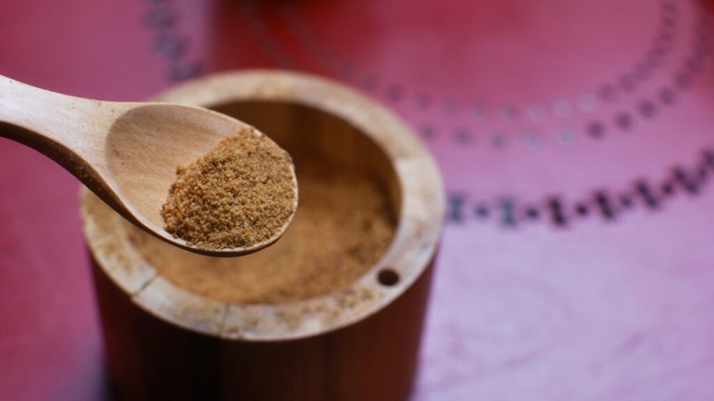 Fine light brown homemade vegan beef-style bouillon powder in a small glass jar with a wooden spoon
