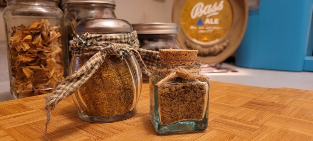 A small glass jar filled with the vibrant Sweet Spicy Garlic Herb All-Purpose Seasoning with a wooden spoon resting near