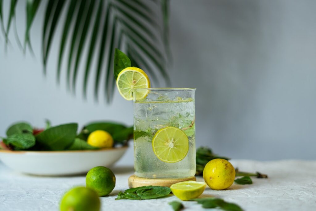 A refreshing glass of clove and lime infused water with whole cloves visible at the bottom and a slice of lime on the ri