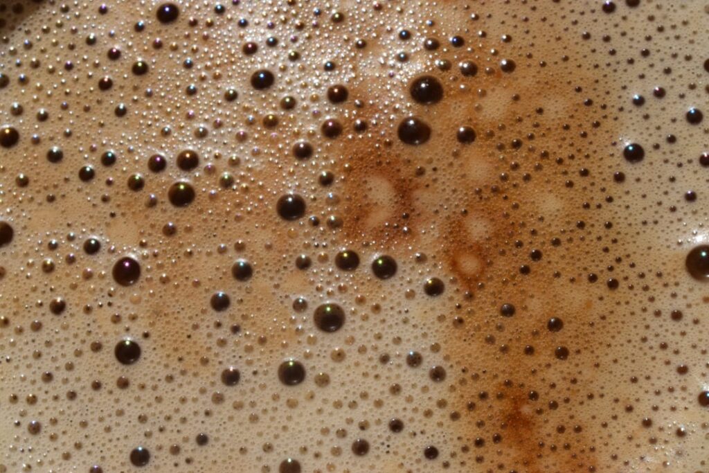 Hands mixing coffee grounds into Vaseline in a small jar