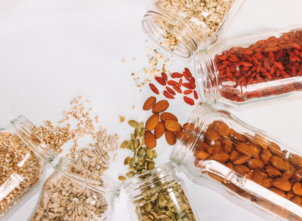 A close-up of a variety of healthy pantry items including olive oil nuts seeds and a selection of dried herbs and spices