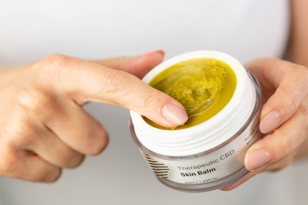 A woman smiling and applying a yellow turmeric and honey face mask to her clean glowing face in a bright bathroom