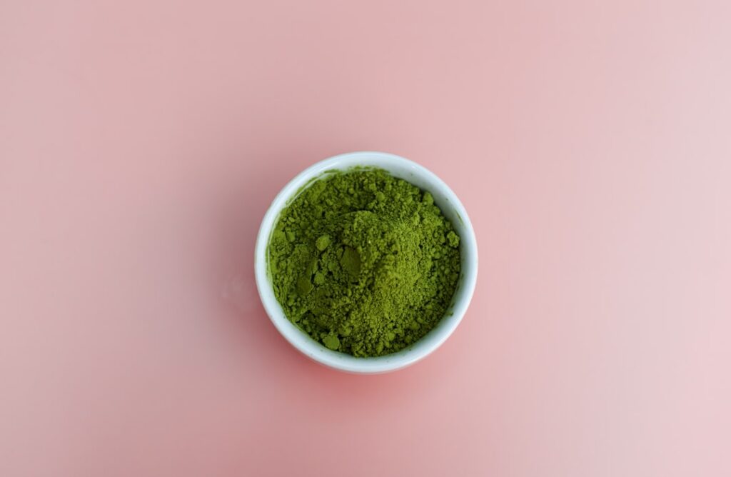 A close-up of vibrant green spirulina powder in a small wooden bowl with a small spoon scooping some The background is s