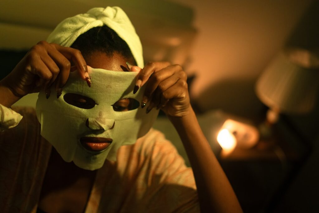 A woman smiling as she applies a green face mask to her clean fresh face Her expression is happy and relaxed in a bright