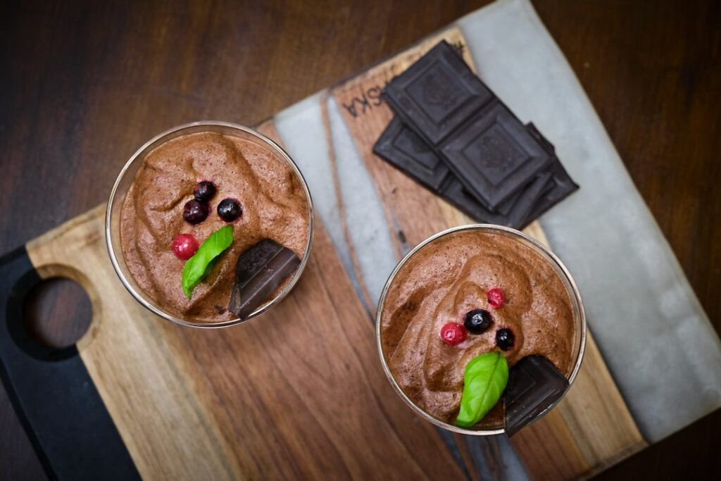 A close-up shot of a creamy rich avocado chocolate mousse served in an elegant glass garnished with fresh raspberries an