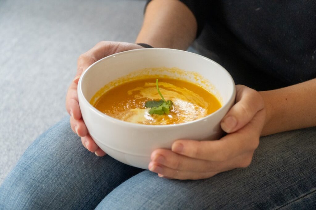 A cozy kitchen scene with a pot of wholesome soup simmering on a stovetop surrounded by fresh vegetables and herbs on a 