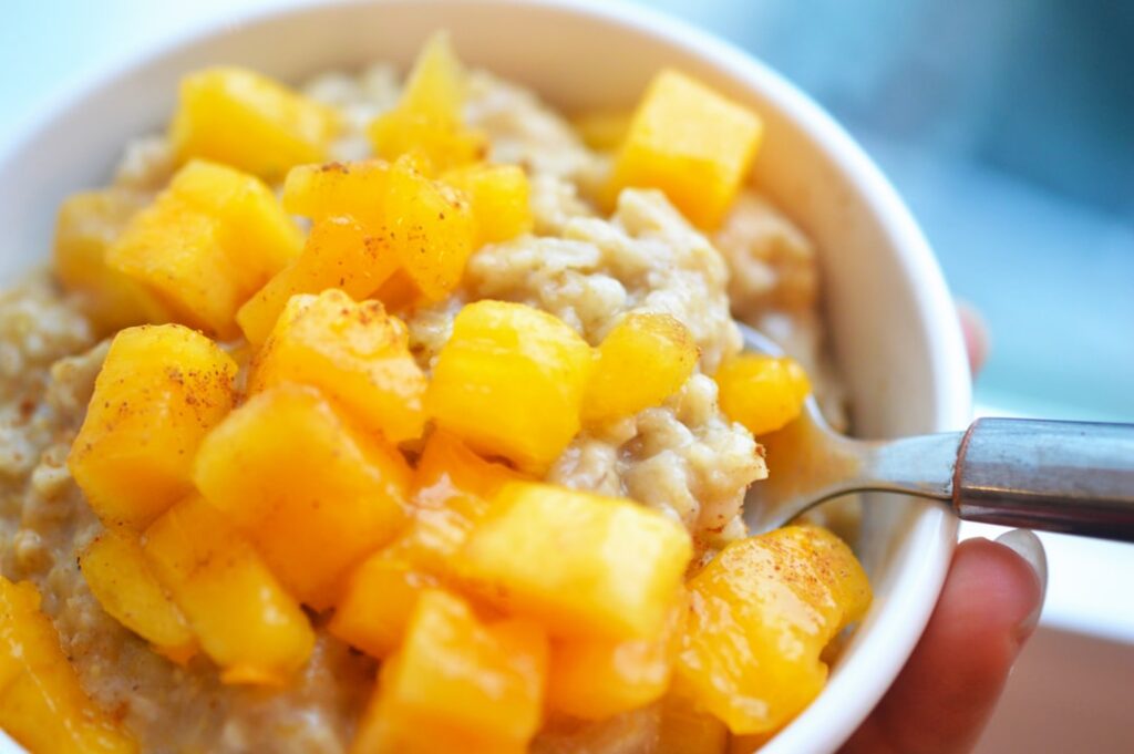 A vibrant bowl of mango sticky oatmeal topped with fresh mango slices toasted coconut flakes and a delicate drizzle of c
