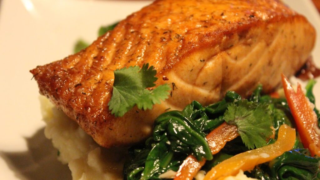 A perfectly cooked teriyaki salmon fillet on a white plate garnished with sesame seeds and chopped green onions Small gl